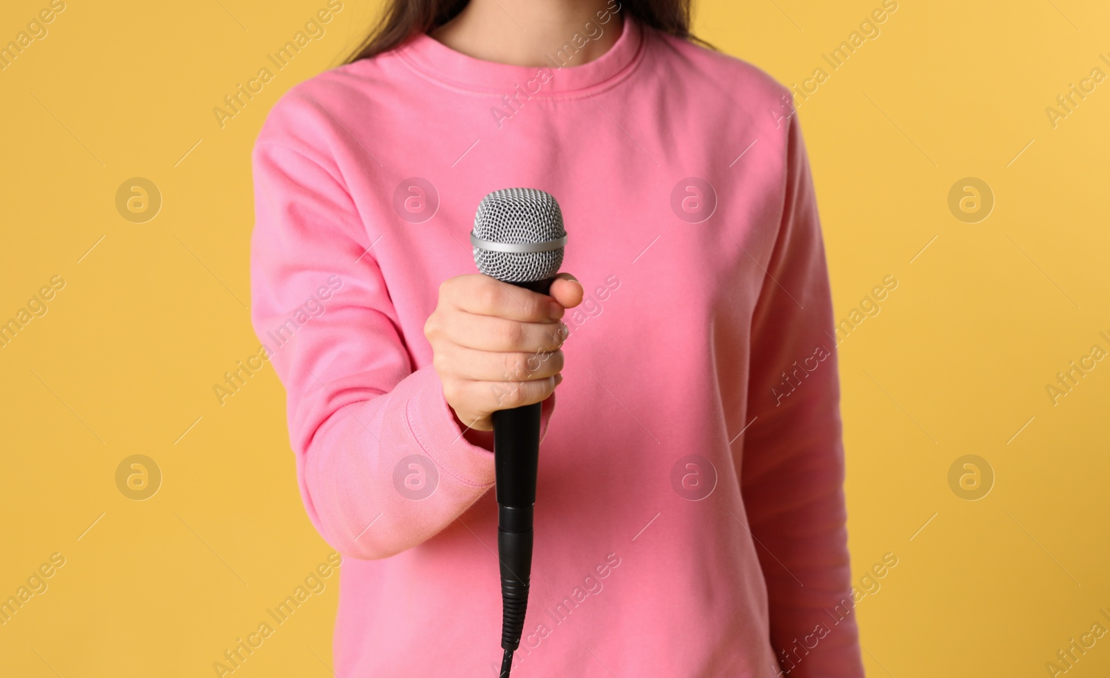 Photo of Young woman holding microphone on color background, closeup view