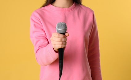 Young woman holding microphone on color background, closeup view