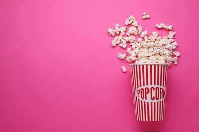 Overturned paper cup with delicious popcorn on pink background, flat lay. Space for text