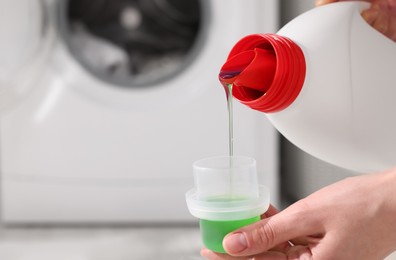 Photo of Woman pouring fabric softener from bottle into cap for washing clothes indoors, closeup. Space for text