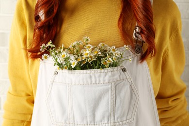 Woman with beautiful tender chamomile flowers in white jumpsuit's pocket, closeup