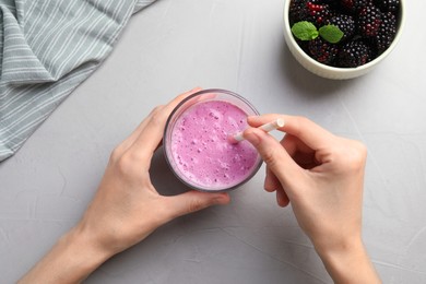 Photo of Woman with glass of delicious blackberry smoothie at white table, top view
