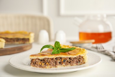 Piece of delicious pie with minced meat on white table indoors