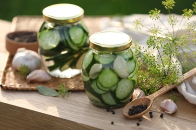 Jars of delicious pickled cucumbers and ingredients on wooden table