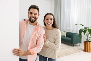 Photo of Happy couple standing near white wall at home, space for text. Invitation to come in room