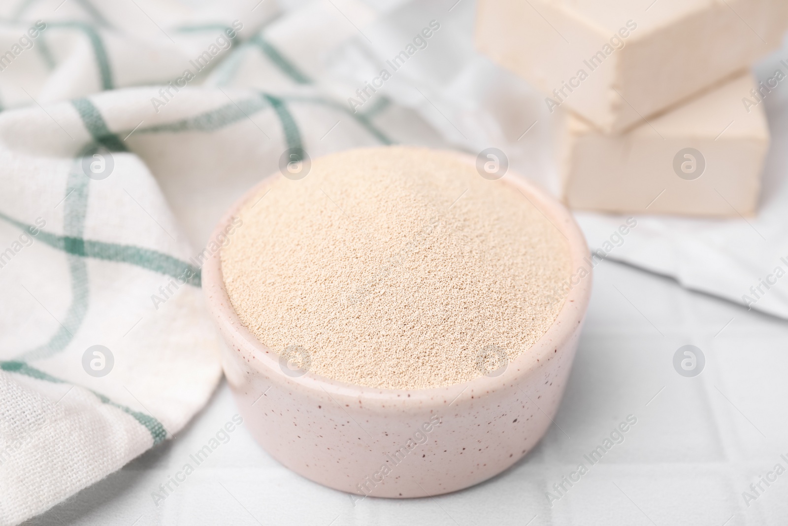 Photo of Granulated yeast in bowl on white tiled table, closeup