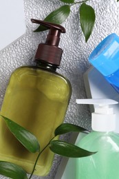 Photo of Different face cleansing products and green leaves on white textured table, flat lay