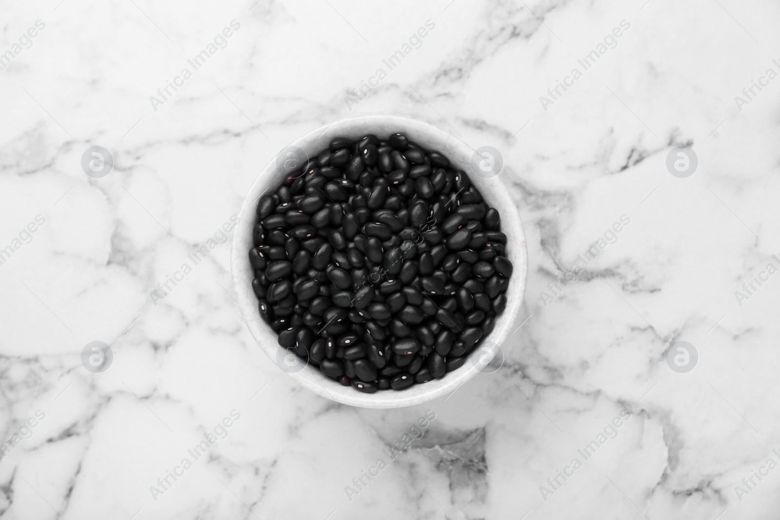 Photo of Bowl of raw black beans on white marble table, top view