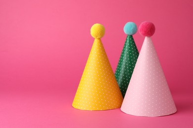 Photo of Beautiful party hats with pompoms on pink background