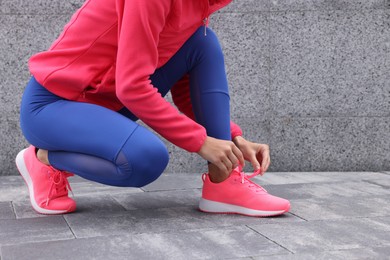 Photo of Woman in gym clothes tying shoelace of sneakers on street, closeup