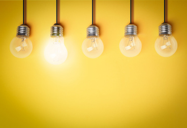 Image of Idea concept. Glowing light bulb among others on yellow background, space for text 