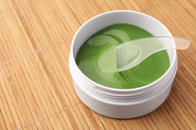 Photo of Jar of under eye patches with spoon on bamboo background, closeup and space for text. Cosmetic product