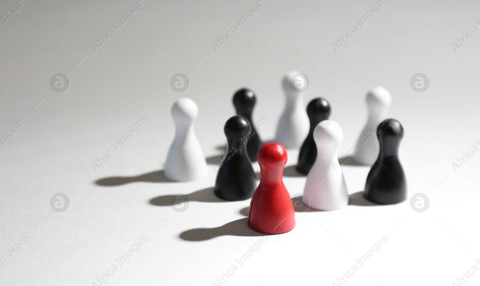 Photo of Red game piece among black and white ones on light grey background. Career promotion concept