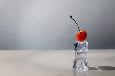 Photo of Sweet ripe cherry and stacked ice cubes on beige table, space for text