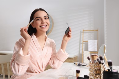 Beautiful young woman applying eyeshadow with brush at dressing table indoors. Space for text