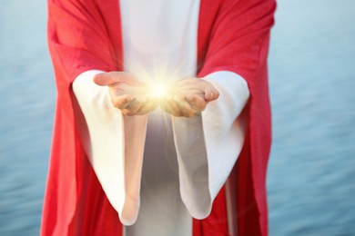 Jesus Christ near water outdoors, closeup. Miraculous light in hands