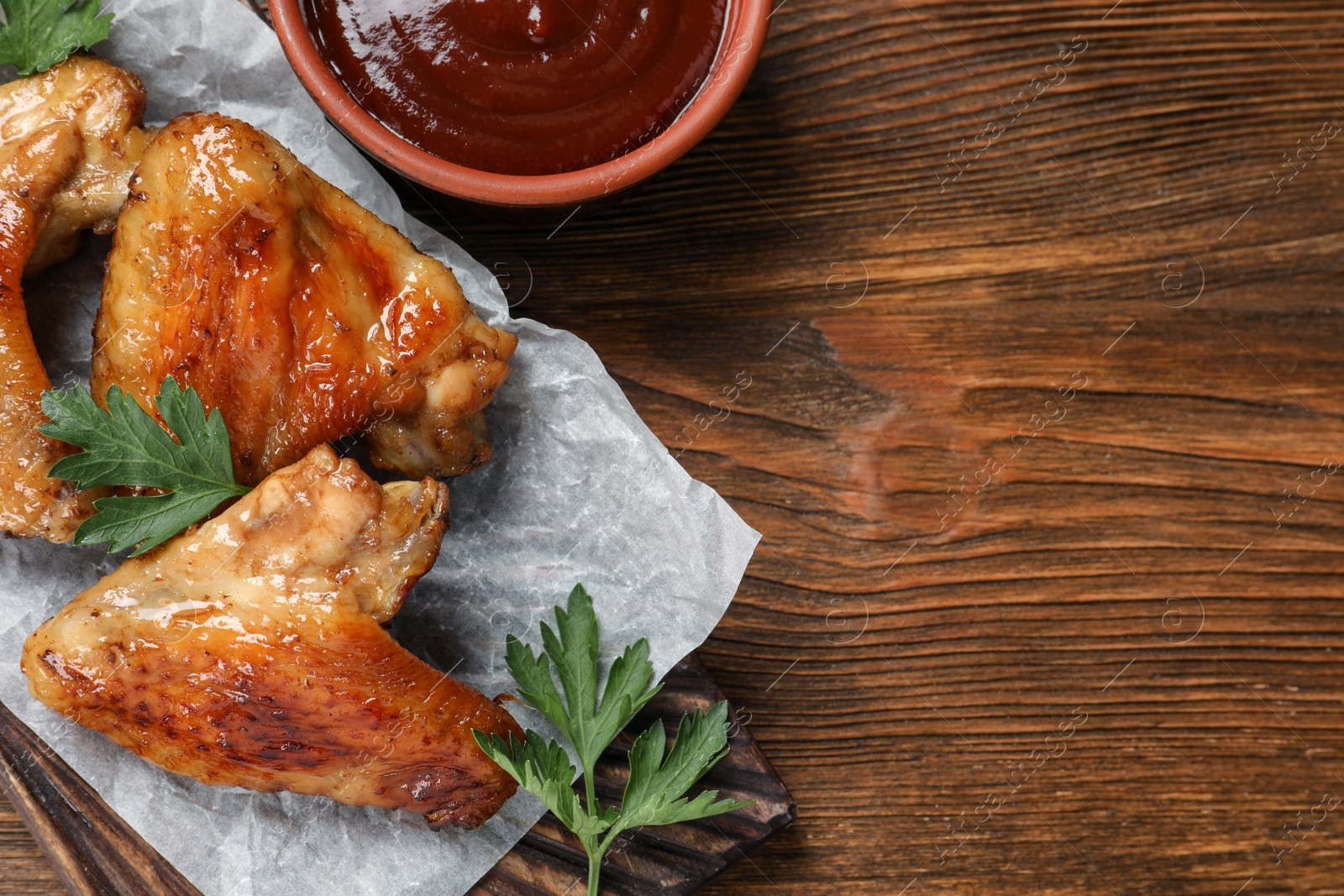 Photo of Delicious fried chicken wings and tomato sauce on wooden table, top view. Space for text