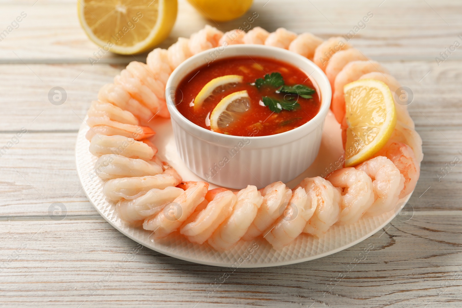 Photo of Tasty boiled shrimps with cocktail sauce and lemon on white wooden table