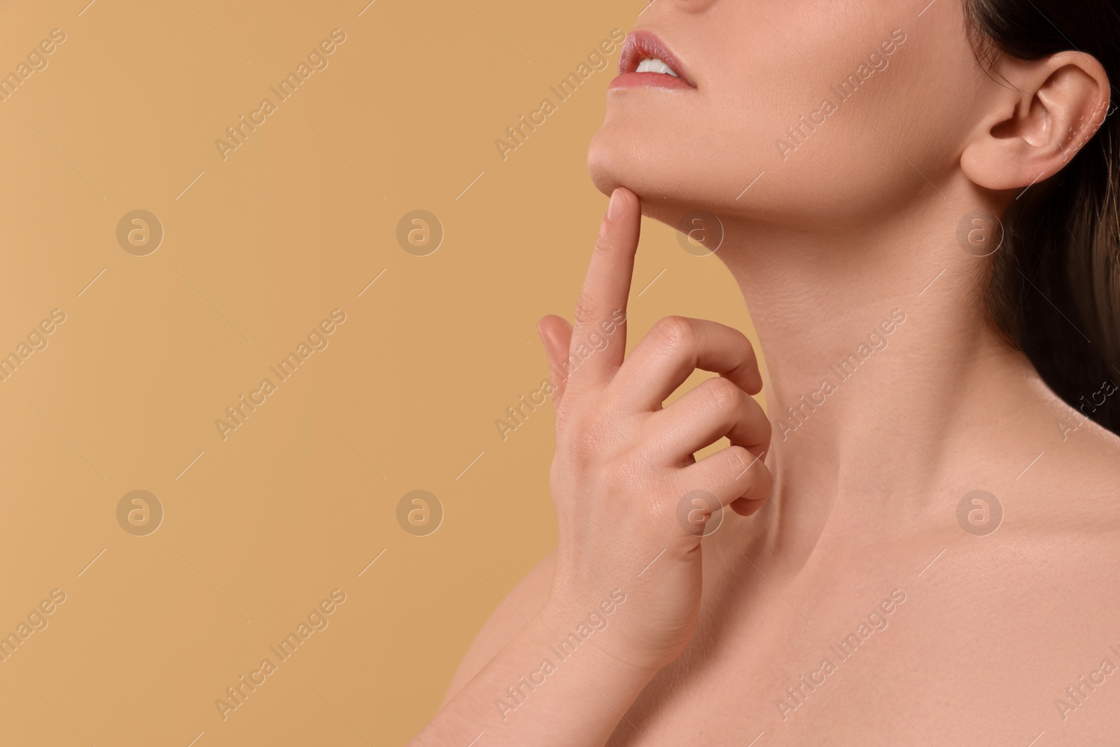 Photo of Young woman massaging her face on beige background, closeup. Space for text