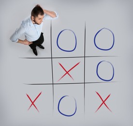 Image of Man and illustration of tic-tac-toe game on grey background, above view. Business strategy concept 