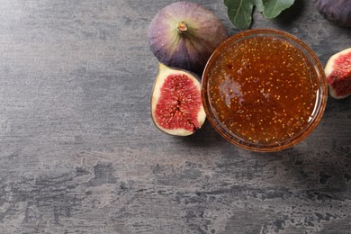 Photo of Bowl with tasty sweet jam and fresh figs on grey table, flat lay. Space for text