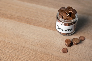 Photo of Glass jar with money and label DONATE on wooden background. Space for text