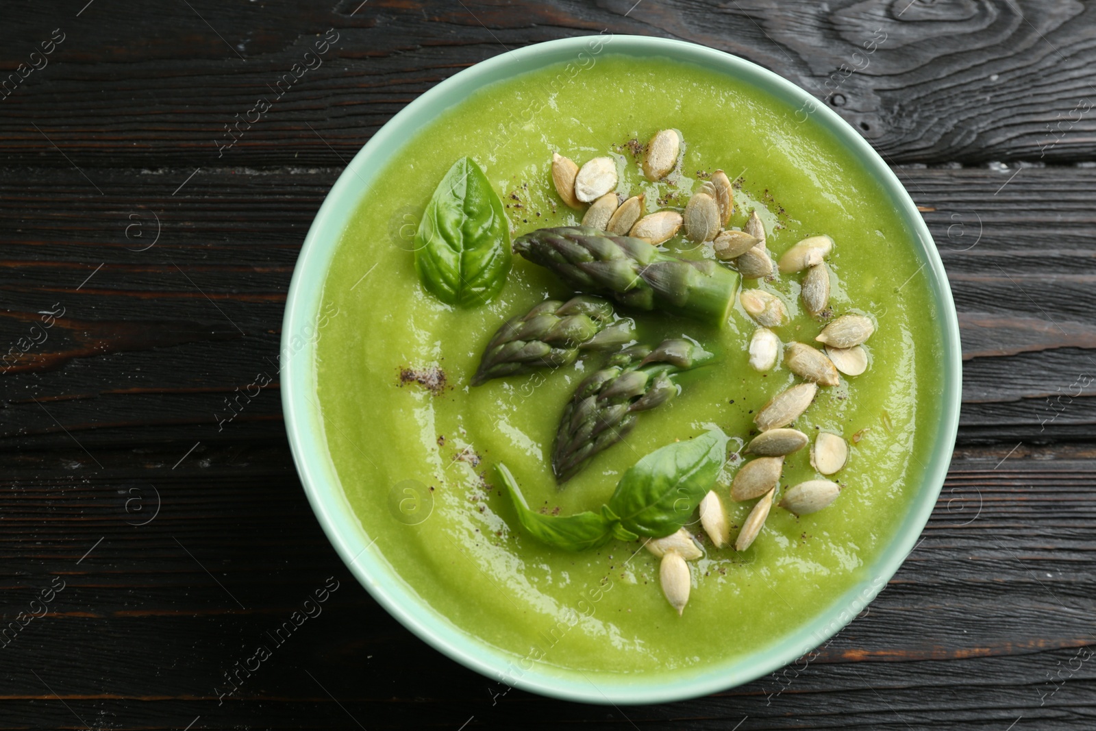 Photo of Delicious asparagus soup in bowl on black wooden table, top view