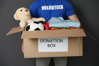 Photo of Male volunteer holding box with donations on grey background