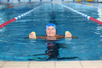 Sportive senior man doing exercises in indoor swimming pool