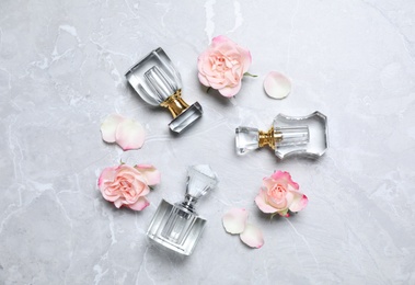 Photo of Bottles of perfume and beautiful flowers on light grey background, flat lay
