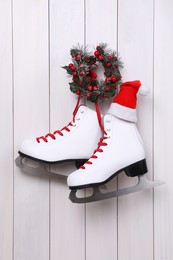 Pair of ice skates with Santa hat and Christmas wreath hanging on white wooden wall