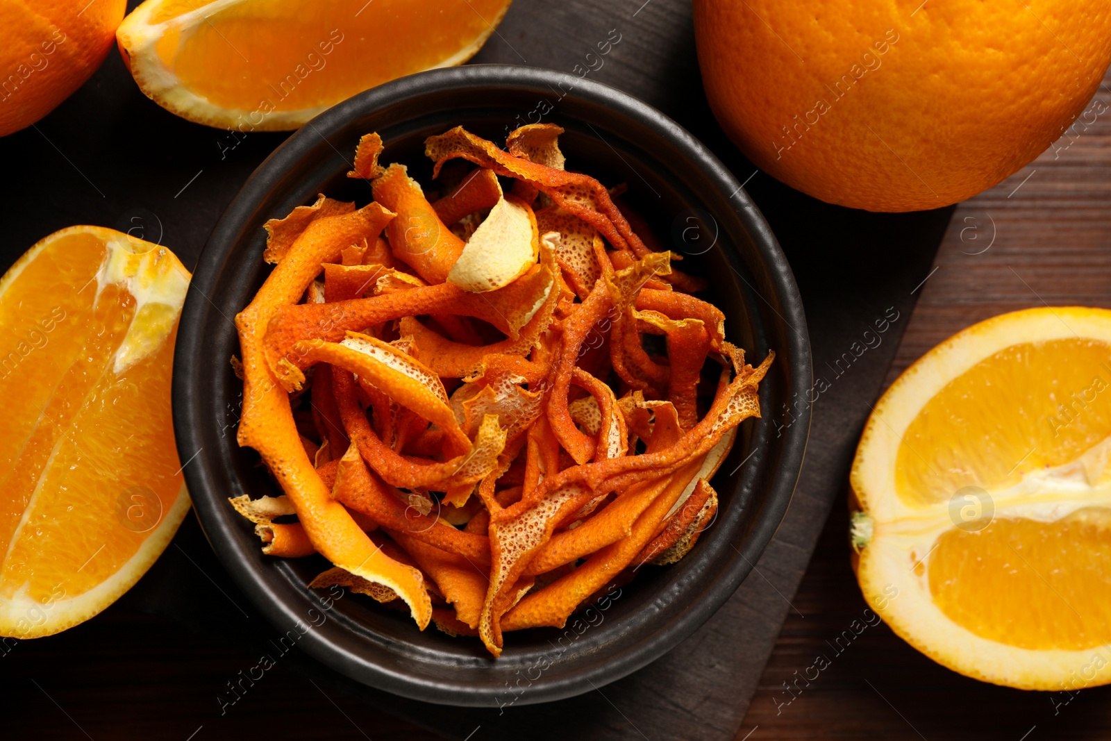 Photo of Bowl with dry orange peels and fresh fruits on wooden table, flat lay