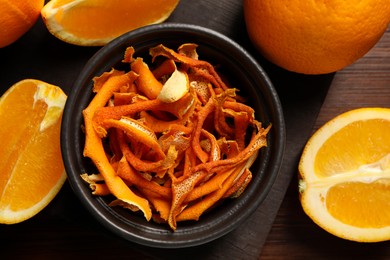 Photo of Bowl with dry orange peels and fresh fruits on wooden table, flat lay