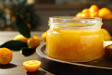 Photo of Delicious kumquat jam in jar on wooden table, closeup