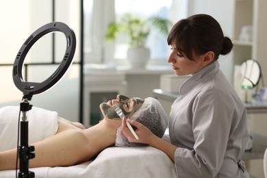 Photo of Cosmetologist applying mask on woman's face in clinic