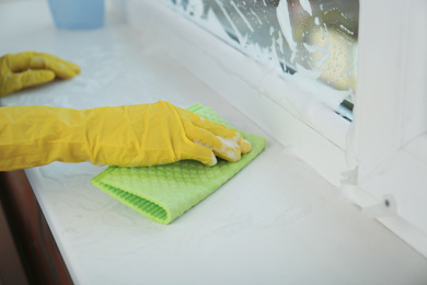 Photo of Woman cleaning window sill with rag, closeup