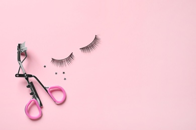 Photo of False eyelashes and curler on pink background, flat lay. space for text