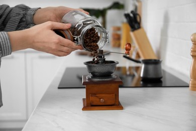Photo of Woman pouring coffee beans into vintage grinder at countertop indoors, closeup