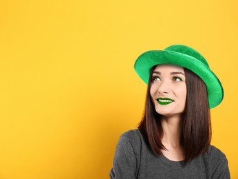 Image of St. Patrick's day party. Pretty woman with green lips in leprechaun hat on golden background. Space for text