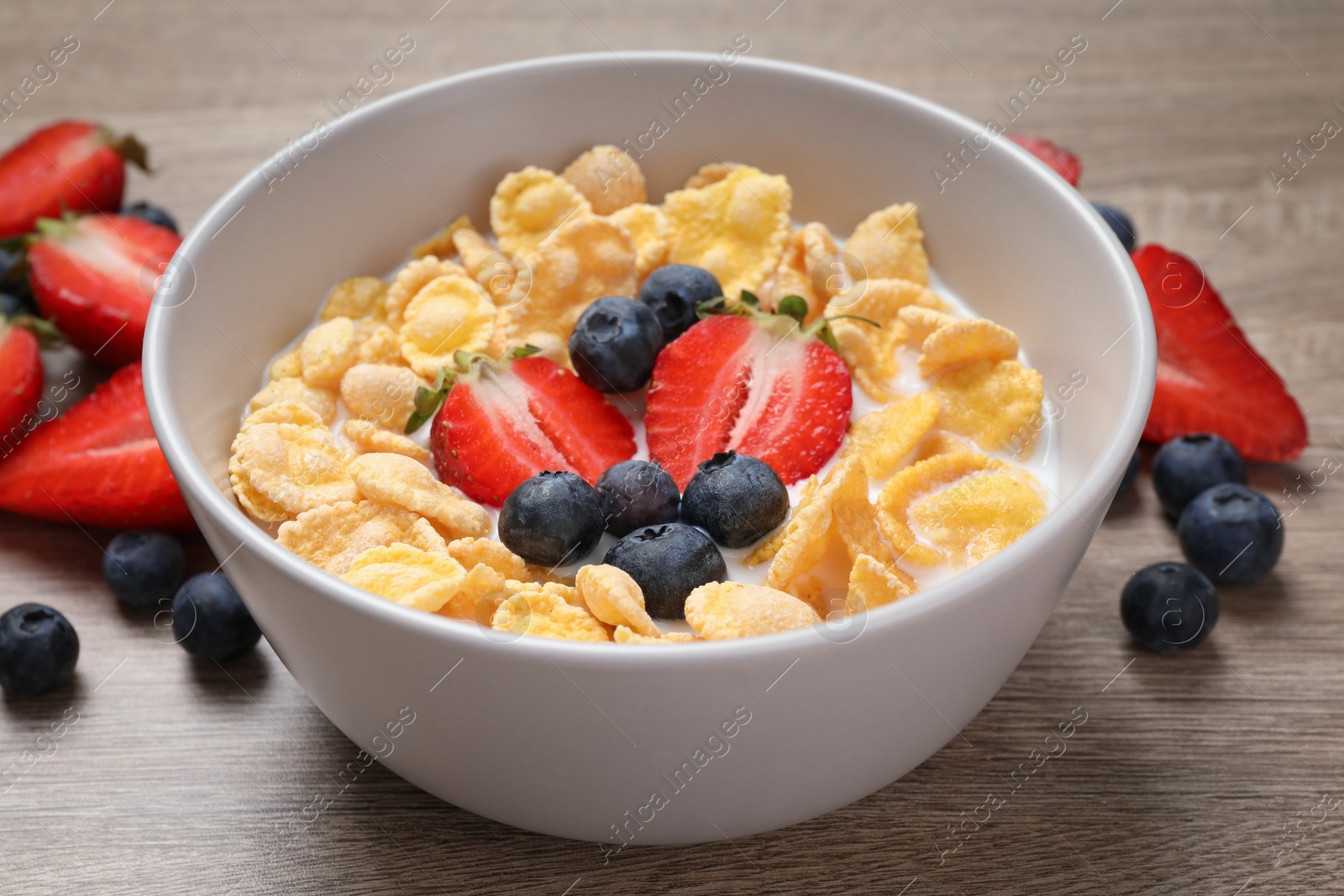 Photo of Delicious crispy cornflakes with milk and fresh berries on wooden table, closeup