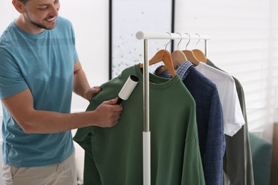 Photo of Man cleaning clothes with lint roller indoors, closeup