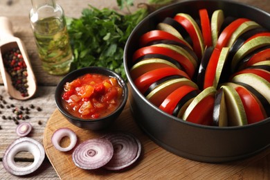Photo of Cooking delicious ratatouille. Different fresh vegetables, and round baking pan on wooden table, closeup