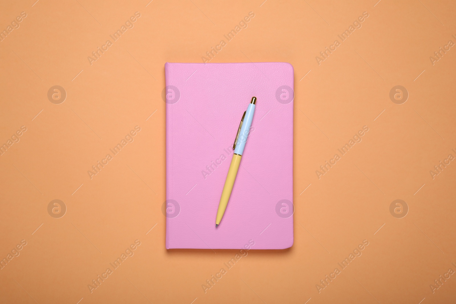 Photo of Closed pink office notebook on pale orange background, top view