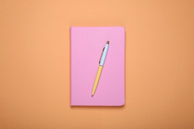 Photo of Closed pink office notebook on pale orange background, top view