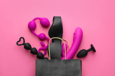 Photo of Shopping bag with different sex toys on pink background, flat lay