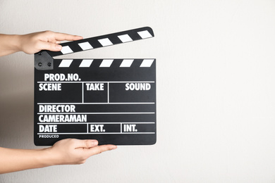 Photo of Woman holding clapperboard against light wall, closeup with space for text. Cinema production