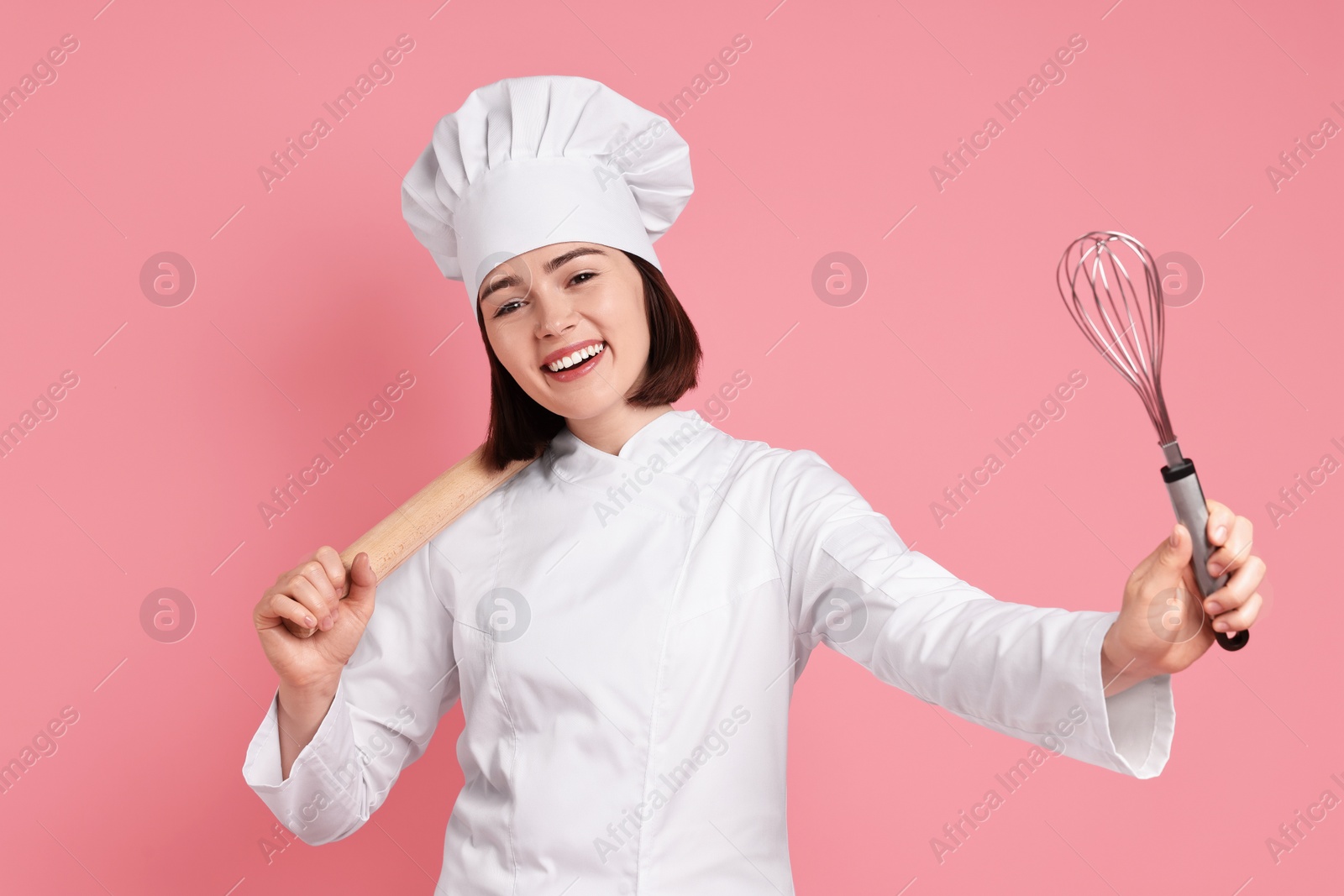 Photo of Happy confectioner with rolling pin and whisk on pink background