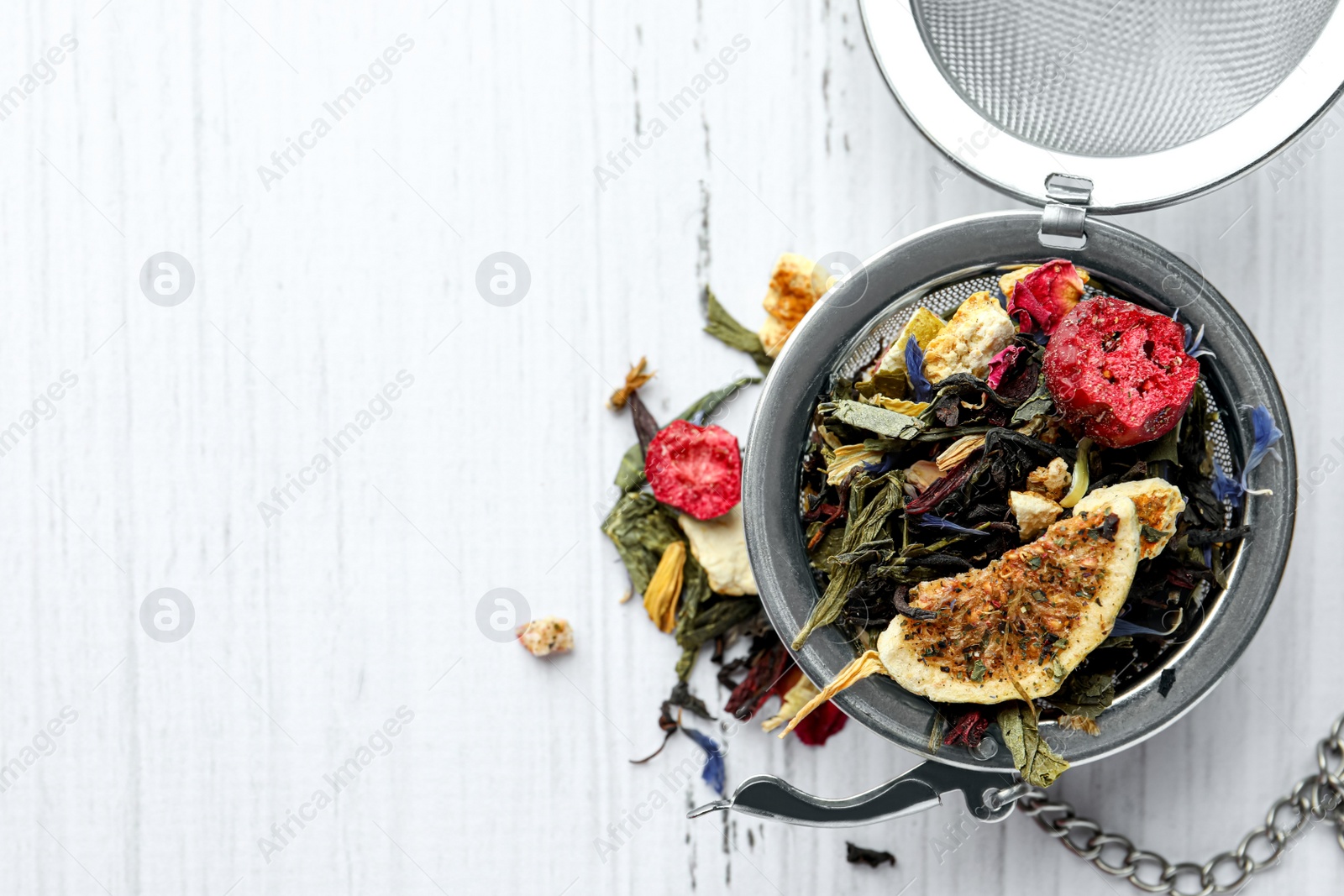 Photo of Snap infuser with dried herbal tea leaves and fruits on white wooden table, top view. Space for text