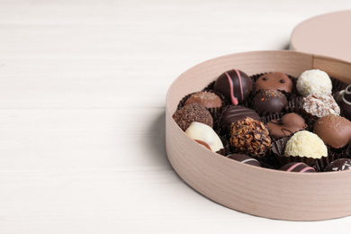 Photo of Box with tasty chocolate candies on white wooden table. Space for text