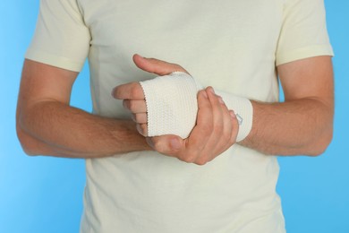 Photo of Man with hand wrapped in medical bandage on light blue background, closeup